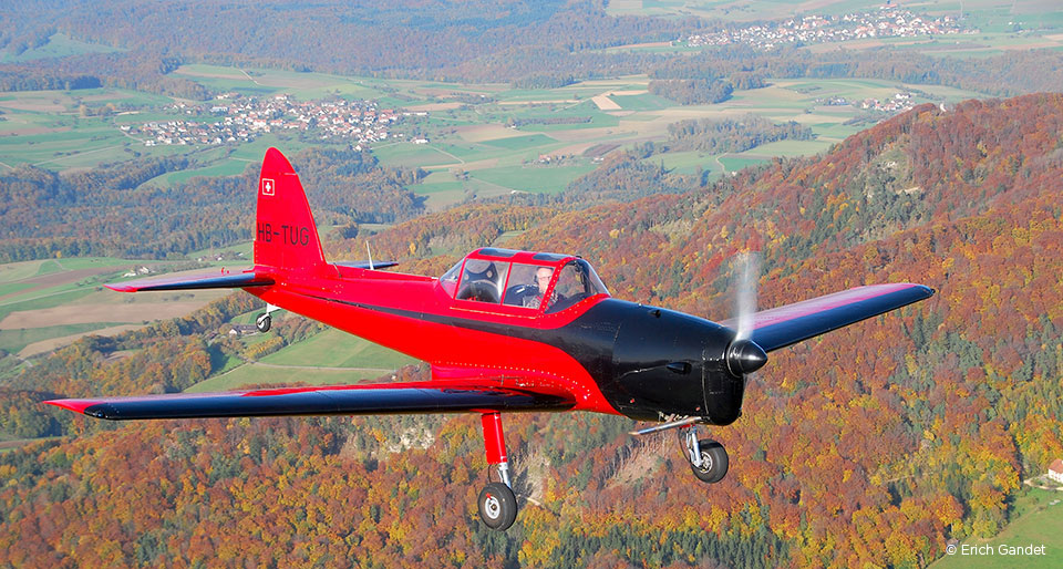 Rot-schwarzes Oldtimerflugzeug über herbstlicher Landschaft